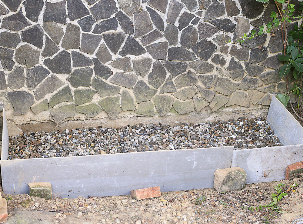 Steny základovej jamy obložíme drevenými alebo cementotrieskovými doskami, vložíme záhradnícku textíliu a nasypeme kamene v hrúbke asi 10 cm.
