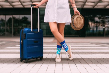 Žena v modrých ponožkách a sukni čakajúca s kufrom