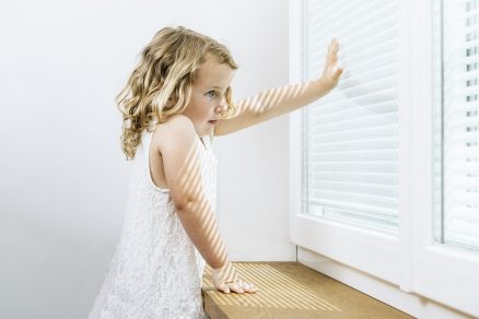 Dievčatko sa drží okna so žalúziou