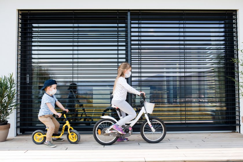 Deti na bicykloch pred domom so žalúziami