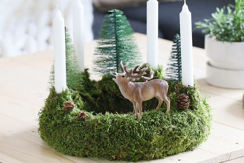 Jednoduchý adventný veniec s machom, bielymi sviečkami a dekoráciami v tvare stromov a jeleňa