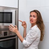 Žena stojaca pri otvorenej mikrovlnke sklamane pozerá a ukazuje na výsledok varenia