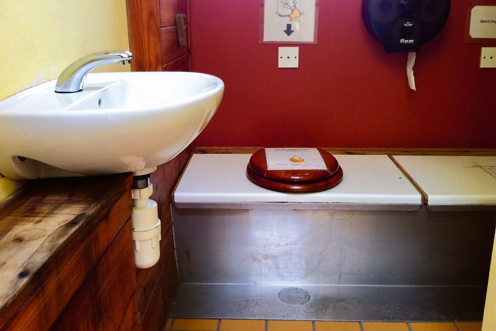 Kompostovacie WC v rodinnom dome vo Walese s dvomi kompostovacími nádobami. Sedadlo sa po naplnení prvej nádoby prehodí nad druhú.