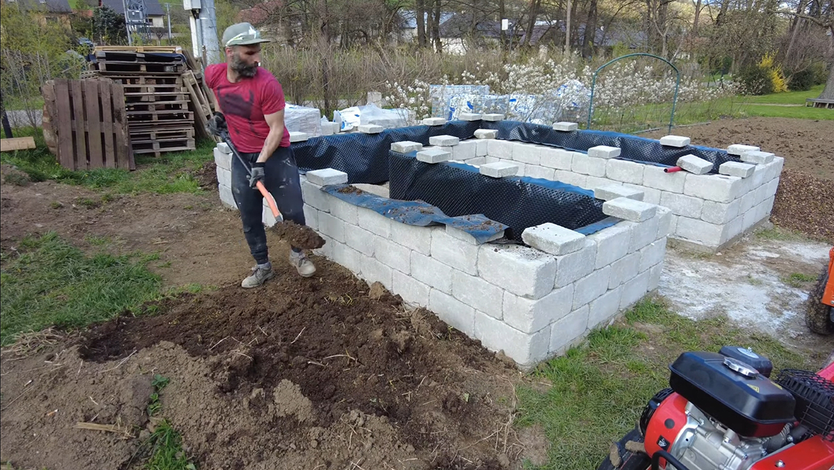 Keď máte fóliu v záhone, môžete sa pustiť do jeho plnenia. Začnite jednou vrstvou zeminy s hrúbkou 15 centimetrov. 