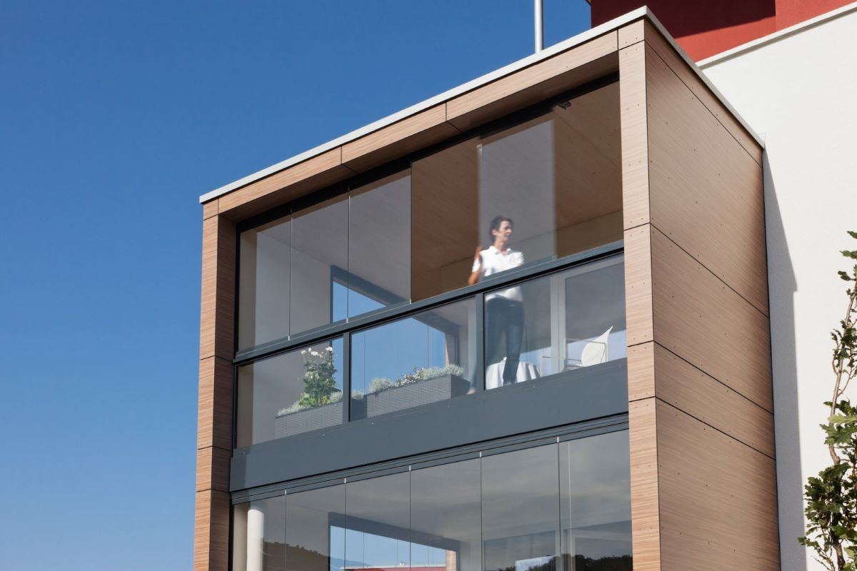 Žena na zasklenom balkóne so skladacím systémom okien.