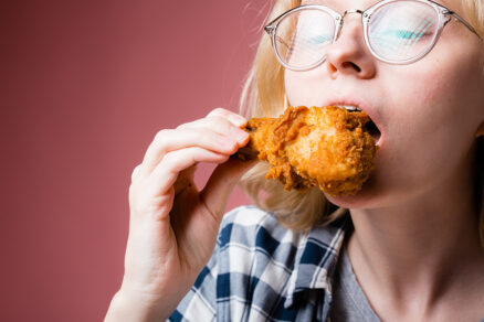 Mladá žena si pochutnáva na vyprážanom kuracom stehienku