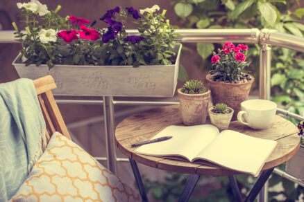 Rozkvitnutá terasa s letničkami v kvetináčoch a šálkou kávy na stole ako oáza pokoja.
